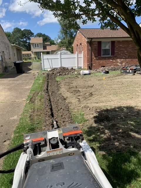 Long drainage trench being installed beside a driveway