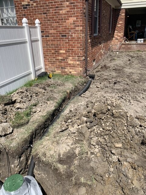 Downspout line and catch basin installation beside a brick home